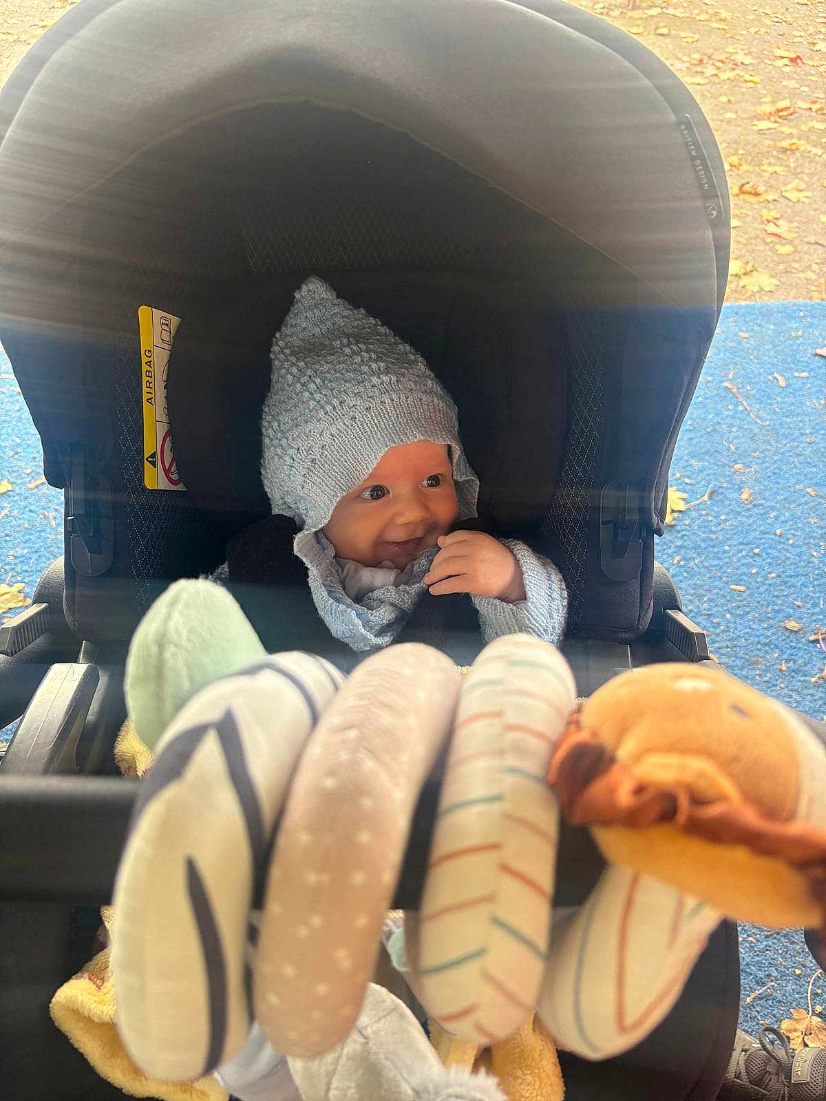 Elio joined the competition — help win amazing prizes! baby, stroller, knit_hat, toy, autumn, outdoor, child, smile, playground, fall_leaves, cozy, seat, infant, warm_clothing, hand, face, headwear, fabric, childhood, cute