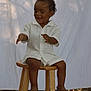 Khalil joined the competition — help win amazing prizes! toddler, child, smiling, sitting, wooden_stool, white_clothing, sandals, outdoor, playful, curly_hair, background_cloth, nature, leaves, texture, portrait, person, happy, young_child, cute, daylight