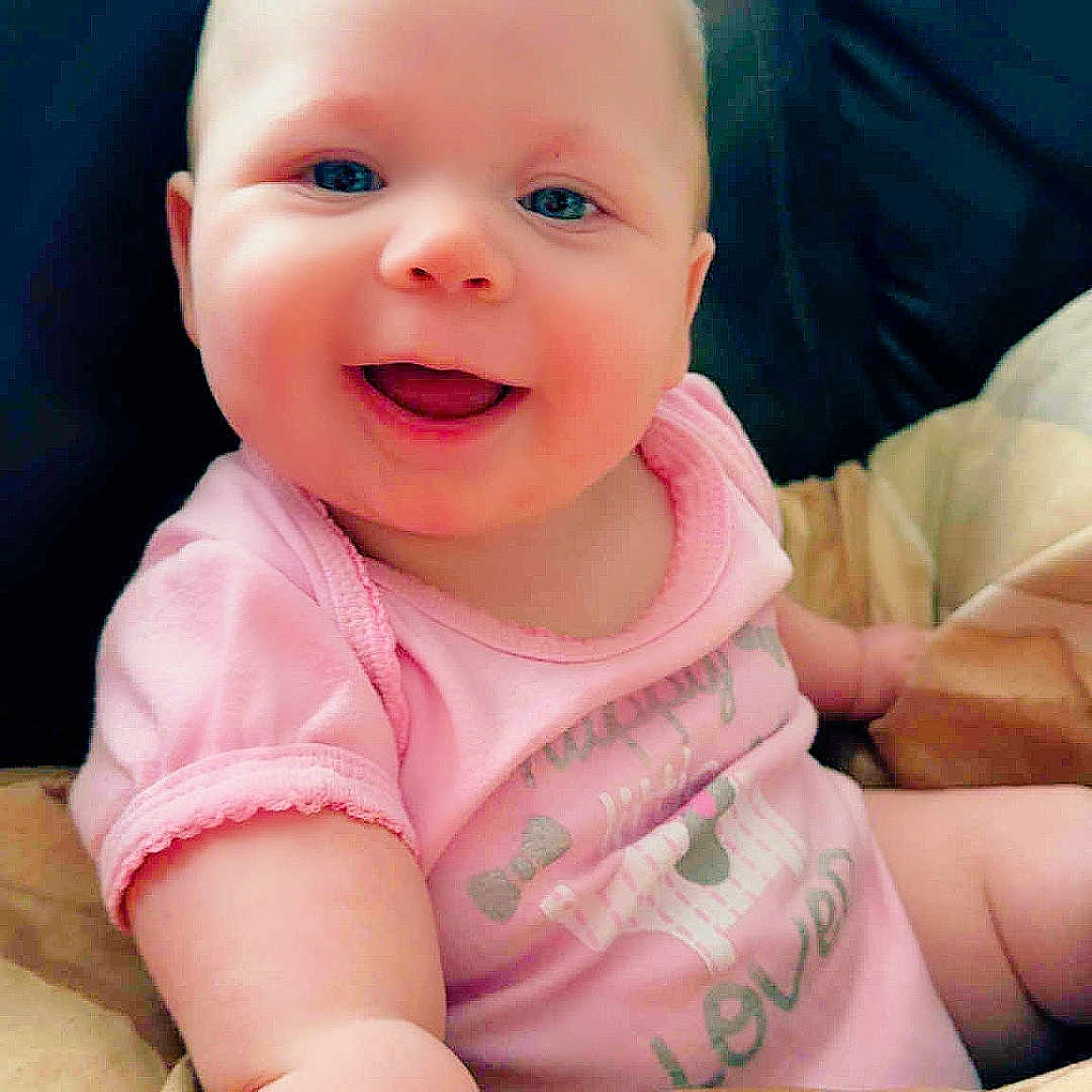 Giavonna is registered to the contest to win money with this photo: arm, baby, blanket, child, comfort, couch, cute, expression, face, happy, indoor, infant, person, pink_onesie, portrait, seated, skin, smiling, soft, young