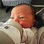 Remy is registered to the contest to win money with this photo: baby, newborn, feeding, bottle, milk, infant, closeup, face, hand, tattoo, arm, white_clothing, indoor, carpet, crib, resting, cute, child, person, newborn_baby