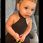 Amora Lei' is registered to the contest to win money with this photo: toddler, child, baby, black_outfit, pink_bows, toy, couch, gray_furniture, curly_hair, baby_hairs, earrings, indoor, portrait, cute, sitting, small_hands, expression, looking_away, soft_lighting, casual