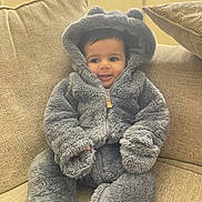 Faisal joined the competition — help win amazing prizes! baby, child, couch, cozy, cute, face, furniture, gray_clothing, happy, hood, indoors, person, plush_suit, seated, sitting, smiling, soft_texture, warm_clothing, young_child, zipper