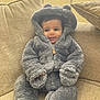 baby, child, couch, cozy, cute, face, furniture, gray_clothing, happy, hood, indoors, person, plush_suit, seated, sitting, smiling, soft_texture, warm_clothing, young_child, zipper