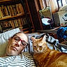 blanket, books, bookshelf, casual, cat, comfort, cozy, furniture, glasses, home, indoor, mirror, orange_tabby, person, pet, reflection, relaxed, resting, striped_shirt, wooden_cabinet