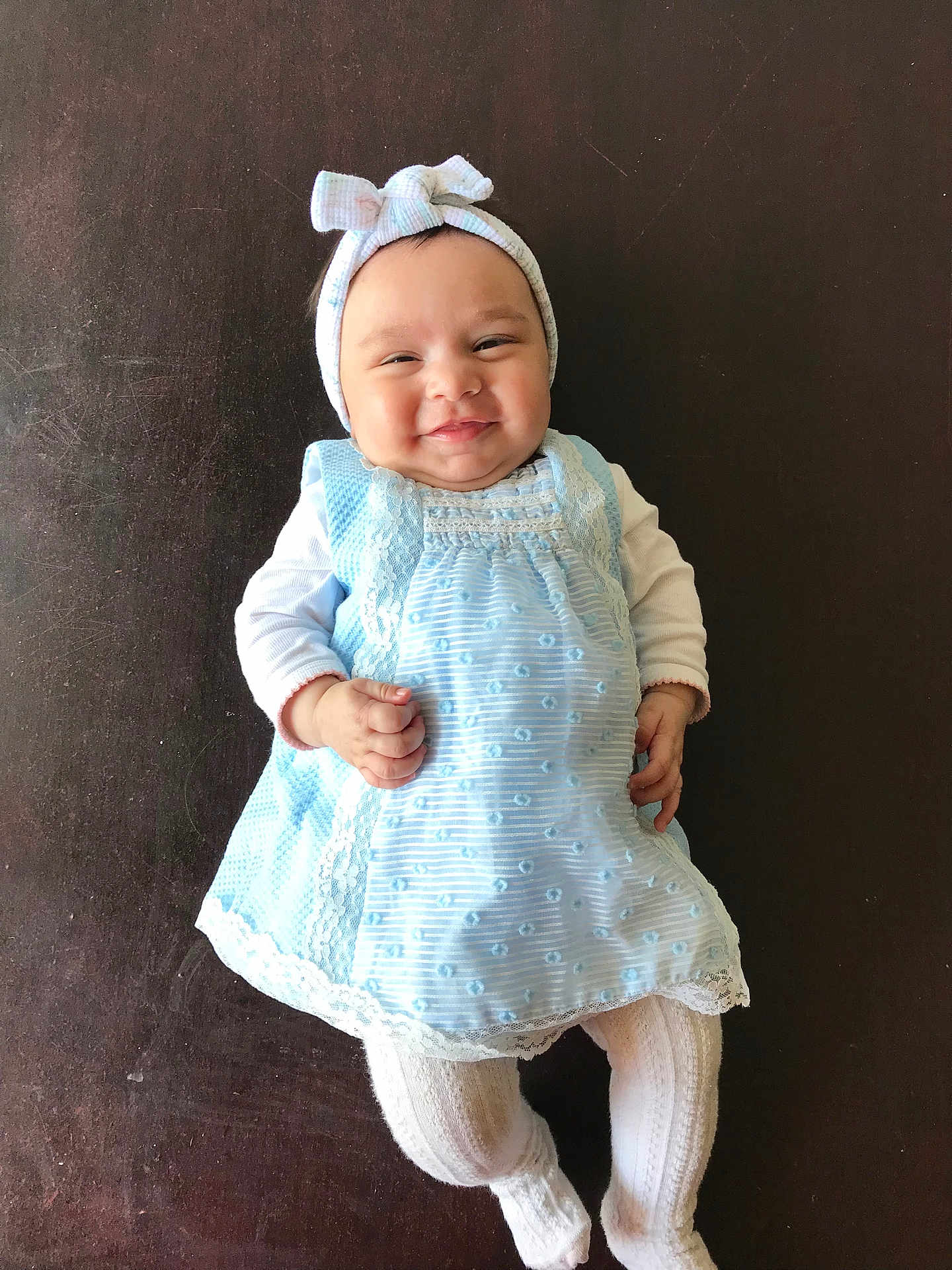 Miryam a rejoint le concours — aidez-le/la à gagner de superbes lots ! baby, infant, smiling, headband, bow, blue_dress, white_tights, lying_down, cute, child, portrait, happy, indoors, person, fashion, baby_clothing, closeup, soft_lighting, background, texture