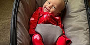 Brynne joined the competition — help win amazing prizes! baby, infant, red_clothing, heart_pattern, baby_seat, smiling, happy, indoor, toy, cushion, face, person, cute, comfort, sleepwear, footwear, carpet, zipper, head, expression