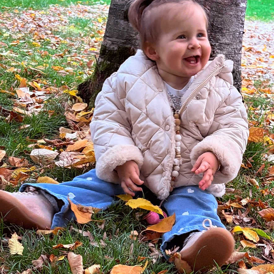 Annaë a rejoint le concours — aidez-le/la à gagner de superbes lots ! autumn, child, clothing, cute, fall, footwear, grass, hairstyle, happy, jacket, leaves, nature, outdoor, pants, park, person, sitting, smile, toddler, tree_trunk