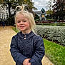 Inaya a rejoint le concours — aidez-le/la à gagner de superbes lots ! child, blonde_hair, smiling, jacket, outdoor, garden, pathway, hedges, statue, autumn, cloudy_sky, park, person, young_child, nature, trees, grass, bench, casual_clothing, portrait