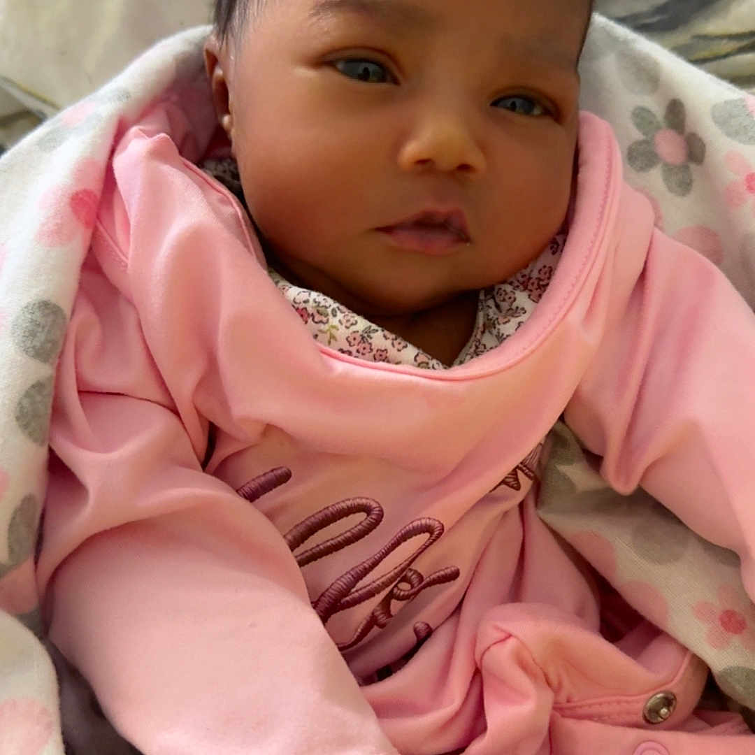 Salah is registered to the contest to win money with this photo: baby, blanket, child, cozy, cute, expression, face, floral_pattern, head, indoors, infant, newborn, pink_clothing, portrait, relaxed, sleepwear, small_hand, soft_lighting, warm, wrapped