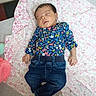 baby, blanket, closed_eyes, cozy, dark_hair, fashionable, floral_shirt, furniture, heart_pattern, indoors, infant, jeans, lying_down, newborn, peaceful, photography, portrait, sleeping, textile, yellow_sock