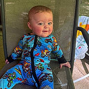 Nicholas is registered to the contest to win money with this photo: baby, child, onesie, motorcycle_print, smile, chair, woven_chair, indoor, portrait, happy, infant, cute, blue_clothing, hand, face, seat, relaxed, home, daylight, baby_gear