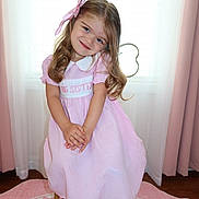 Deniz is registered to the contest to win money with this photo: child, girl, pink_dress, bow, smile, sitting, stool, curtains, window, indoors, carpet, happy, cute, portrait, person, long_hair, white_shoes, floor, home, young