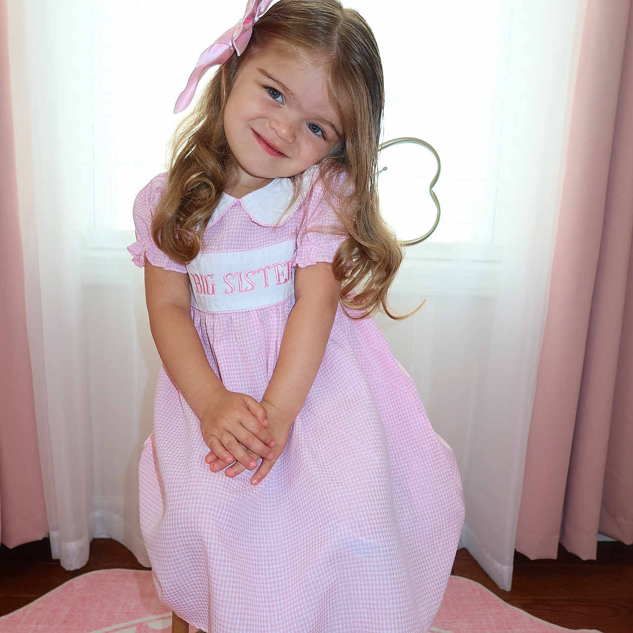 Deniz is registered to the contest to win money with this photo: child, girl, pink_dress, bow, smile, sitting, stool, curtains, window, indoors, carpet, happy, cute, portrait, person, long_hair, white_shoes, floor, home, young