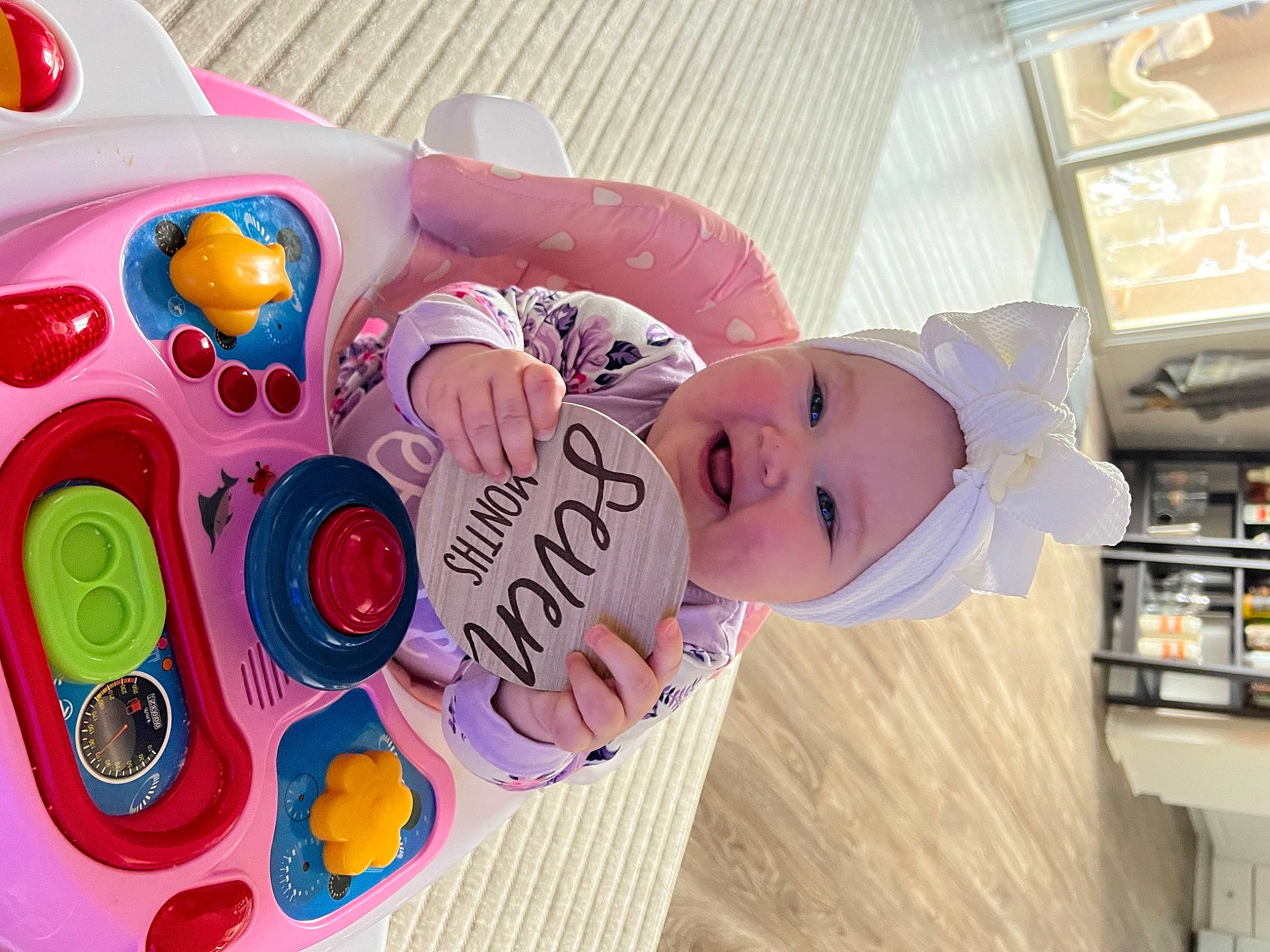 Emry is registered to the contest to win money with this photo: baby, baby_products, baby_toddler_clothing, baby_toys, bookcase, carmine, child, font, fun, happy, hat, headwear, magenta, party_supply, person, pink, plastic, play, shelf, smile
