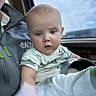 baby, infant, child, person, face, blue_eyes, short_hair, clothing, shirt, car_interior, window, sky, clouds, adult_partial, lap, hand, expression, portrait, seat, casual