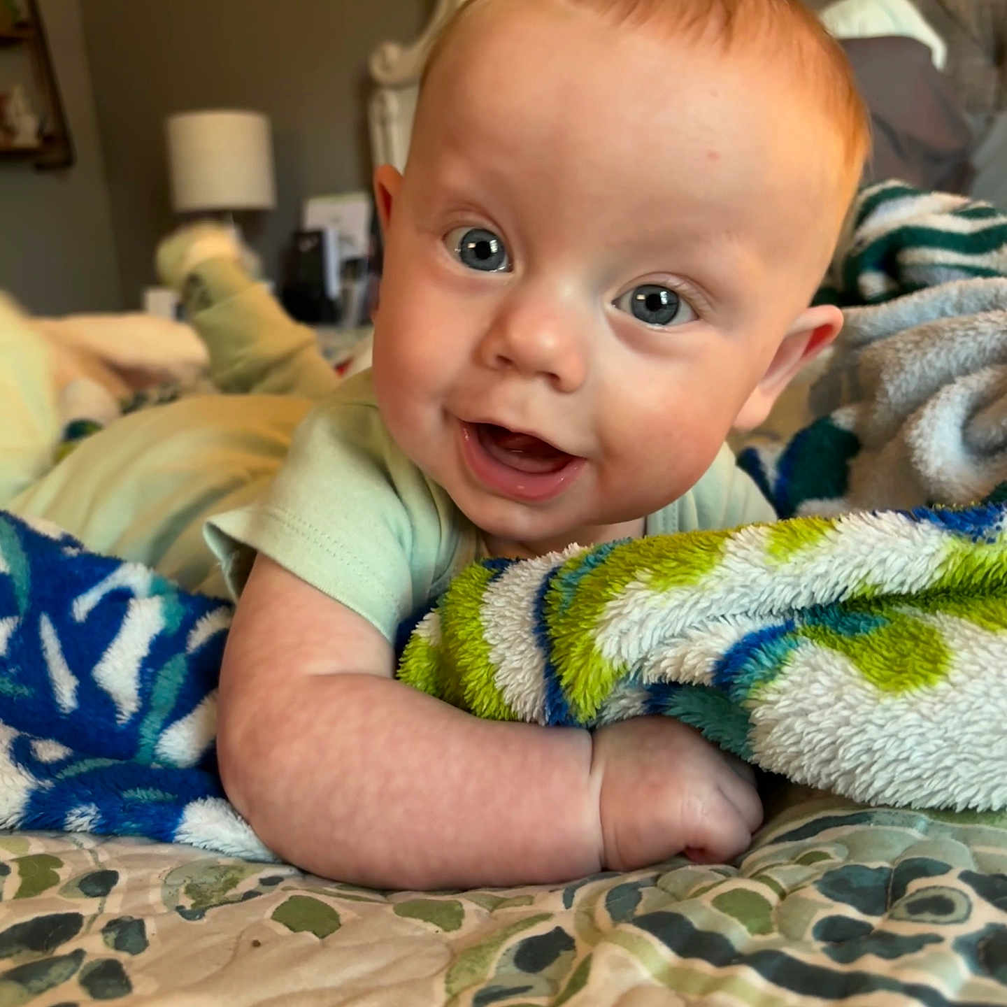 Kyle is registered to the contest to win money with this photo: baby, bed, blanket, blue_eyes, child, clothing, cozy, cute, face, fun, happy, head, home, indoor, infant, person, portrait, skin, smiling, toddler