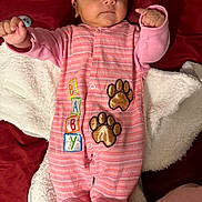 Elaine is registered to the contest to win money with this photo: baby, infant, pink_clothing, onesie, hat, blanket, paw_prints, embroidered, lying_down, curious_expression, indoor, soft_texture, child, newborn, cute, sleepwear, person, portrait, baby_girl, cozy
