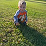 toddler, child, grass, outdoor, park, kneeling, portrait, blue_eyes, cartoon_shirt, long_shadow, sunlight, daytime, bokeh, shallow_depth_of_field, cute, curious, casual_clothing, young_child, face, smiling