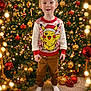 child, boy, christmas_tree, holiday, sweater, pikachu, festive, decorations, ornaments, lights, carpet, sock, mismatched_socks, smile, indoors, celebration, seasonal, red, gold, green