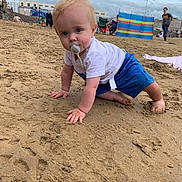 Finley joined the competition — help win amazing prizes! baby, child, pacifier, beach, sand, blue_shorts, white_tshirt, crawling, outdoor, cloudy_sky, people, windbreak, barefoot, playful, summer, vacation, person, footprints, toddler, casual