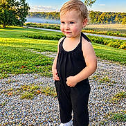 Skylar is registered to the contest to win money with this photo: child, toddler, portrait, outdoor, standing, smiling, black_outfit, white_shoes, gravel, grass, lake, mist, hills, landscape, blue_sky, sunlight, trees, nature, fashion, earrings