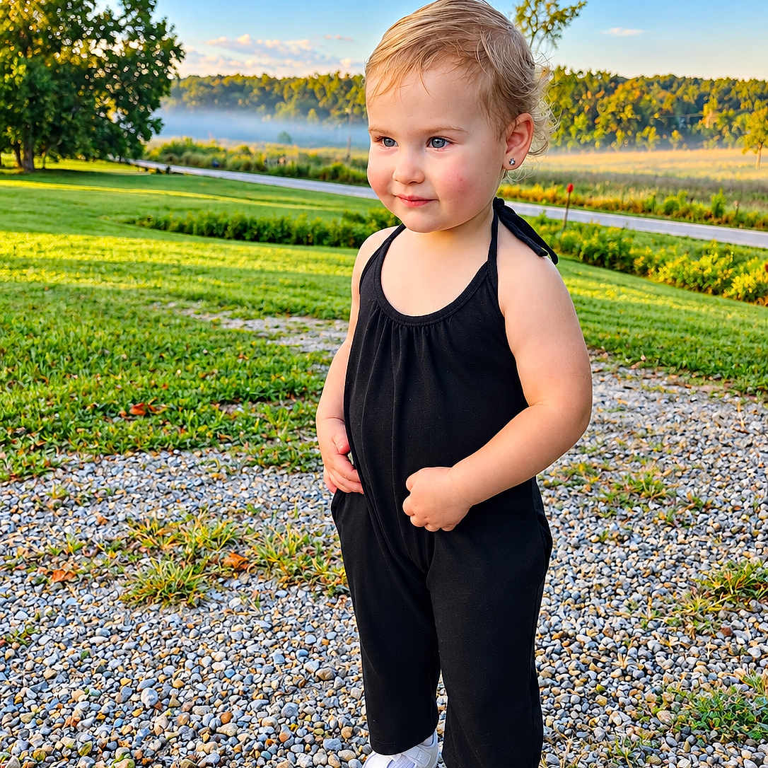 Skylar is registered to the contest to win money with this photo: child, toddler, portrait, outdoor, standing, smiling, black_outfit, white_shoes, gravel, grass, lake, mist, hills, landscape, blue_sky, sunlight, trees, nature, fashion, earrings