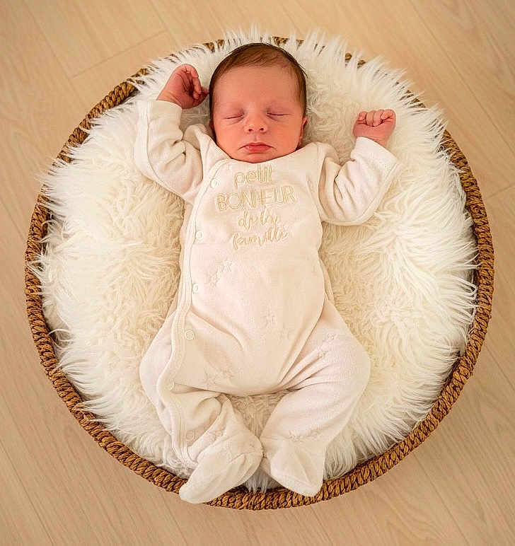 Elyo a rejoint le concours — aidez-le/la à gagner de superbes lots ! baby, newborn, infant, sleeping, onesie, basket, woven_basket, faux_fur, fur_rug, cozy, soft_texture, wood_floor, top_down_view, portrait, peaceful, nursery, tiny, cute, hands_up, white_clothing