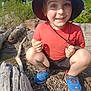 Corbin is registered to the contest to win money with this photo: child, boy, blue_hat, red_shirt, blue_sneakers, outdoor, rocks, tree_log, smiling, crouching, nature, sunlight, playful, ground, summer, happy, person, forest, adventure, exploring
