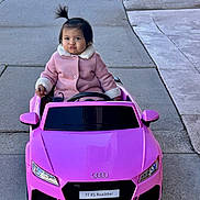 Lia Hernandez joined the competition — help win amazing prizes! toddler, child, toy_car, pink_coat, pony_tail, sidewalk, outdoor, cute, pouty_face, audi, roadster, vehicle, playtime, small_car, person, winter_clothing, concrete, funny_expression, daylight, street