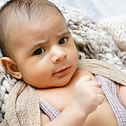 Matias is registered to the contest to win money with this photo: baby, infant, face, eyes, blanket, knit_blanket, hand, ear, skin, portrait, close_up, expression, curious, newborn, wrapped, soft_texture, cozy, bedding, indoors, eyelashes