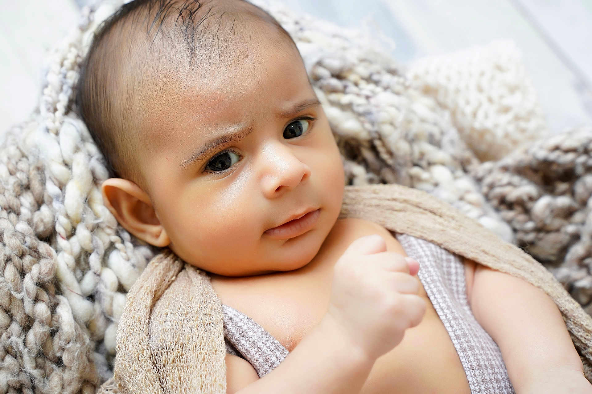 Matias is registered to the contest to win money with this photo: baby, infant, face, eyes, blanket, knit_blanket, hand, ear, skin, portrait, close_up, expression, curious, newborn, wrapped, soft_texture, cozy, bedding, indoors, eyelashes