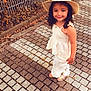 autumn_leaves, brick, casual, child, curly_hair, cute, daylight, fence, girl, happy, hat, nature, outdoor, pavement, portrait, sandals, smile, standing, summer_clothing, young