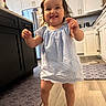 Devani joined the competition — help win amazing prizes! toddler, child, baby, smiling, walking, blue_dress, kitchen, floor, cabinet, rug, barefoot, happy, indoor, person, young_child, wood_floor, appliances, home, cute, playful