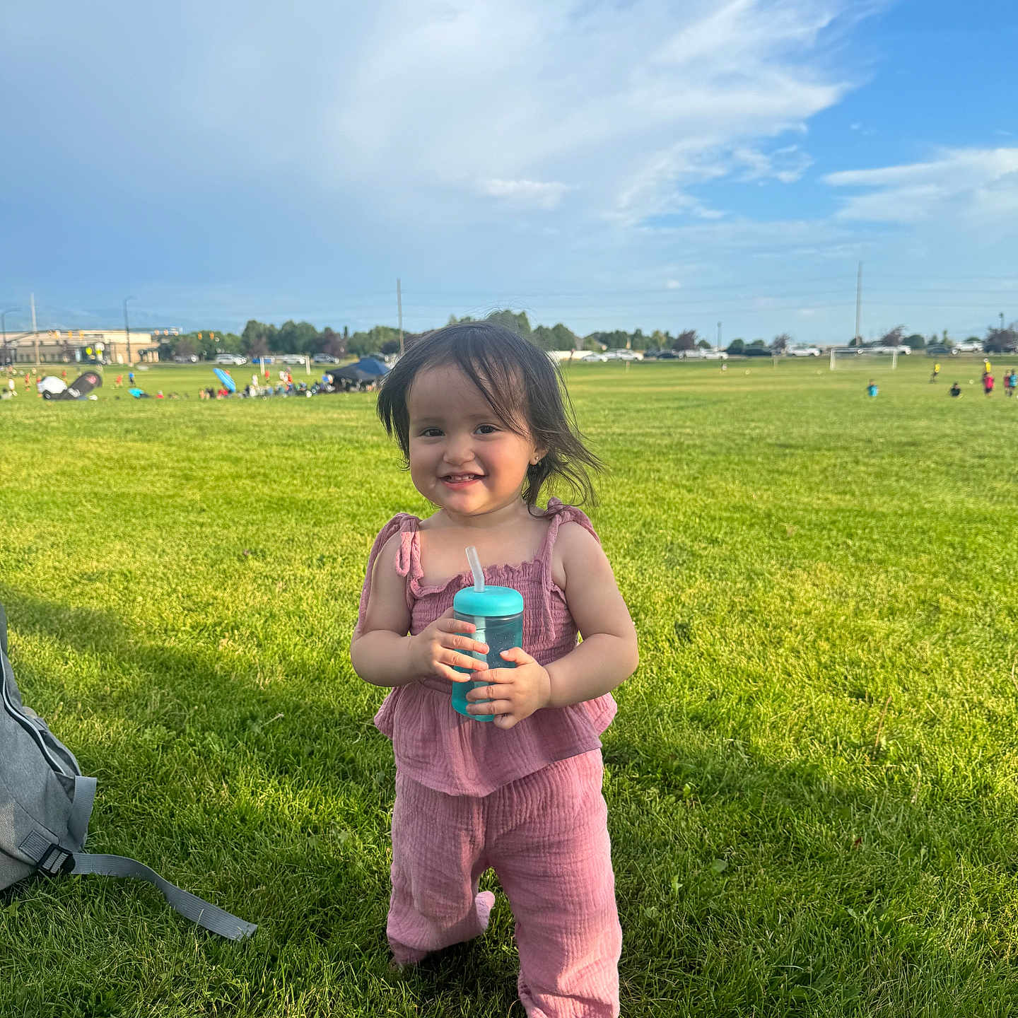 Devani joined the competition — help win amazing prizes! child, toddler, grass, outdoor, blue_sky, clouds, greenery, pink_clothing, barefoot, sippy_cup, smile, happy, playing, daylight, park, field, people, sports, summer, casual
