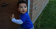 Aaron is registered to the contest to win money with this photo: blue_shirt, brick_wall, casual_clothing, child, curious, daylight, doorway, expression, flooring, grass, looking_back, motion, outdoor, person, playful, short_hair, side_view, small_hand, toddler, young_child