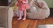 Penelope is registered to the contest to win money with this photo: toddler, child, smiling, indoor, wooden_floor, bean_bag, cookie, furniture, person, home, orange_dress, barefoot, happy, living_room, man, table, background, cozy, casual, daylight
