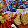 toddler, child, christmas_tree, presents, holiday, red_plaid, wrapped_gifts, wooden_floor, smiling, happy, indoor, festive, decorations, colorful_lights, joyful, person, celebration, seasonal, family, home