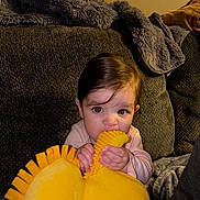 Ava is registered to the contest to win money with this photo: baby, blanket, blue_eyes, brown_hair, child, closeup, couch, face, hands, home, indoor, infant, pink_clothing, plush_toy, portrait, sitting, smiling, sofa, teething, yellow_toy