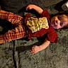 child, toddler, smiling, happy, portrait, lying_down, indoor, blanket, couch, red_shirt, plaid_pants, bear_design, brown_hair, face, hands, legs, cozy, casual_clothing, photography, playful