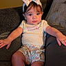 baby, child, infant, sitting, couch, portrait, bow, headband, floral_pattern, outfit, baby_clothing, smiling, wide_eyes, indoors, living_room, furniture, cushion, photography, cute, legs