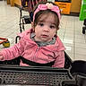 baby, child, toddler, shopping_cart, grocery_store, pink_jacket, headband, flower, sitting, portrait, face, eyes, brown_hair, indoor, retail, store, adult, plaid_shirt, cart, shopping