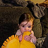 Ava is registered to the contest to win money with this photo: baby, blanket, blue_eyes, brown_hair, chewing, child, couch, cozy, curious, furniture, home, indoors, infant, portrait, sitting, smiling, teething, toy, warm_lighting, yellow_toy