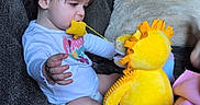Ava is registered to the contest to win money with this photo: child, toddler, baby, sitting, couch, plush_toy, dinosaur, yellow_toy, toy, indoors, living_room, blanket, portrait, face, profile, brown_hair, long_sleeves, playtime, family, cute