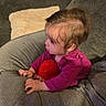 Ava is registered to the contest to win money with this photo: baby, child, toddler, sitting, couch, sofa, cushion, blanket, red_ball, toy, pink_clothing, long_sleeves, brown_hair, profile, indoor, living_room, portrait, hands, relaxed, cozy
