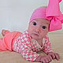 baby, infant, child, pink_bow, headband, checkered_onesie, tummy_time, lying_on_stomach, portrait, wide_eyes, hands, skin, bed_sheet, indoor, cute, newborn, fashion_accessory, hat, pink_clothing, soft_lighting