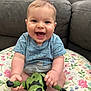 baby, smiling, toy, action_figure, couch, cushion, indoor, child, happy, shirt, blue_shirt, hand, face, person, sitting, playful, infant, young_child, home, cute