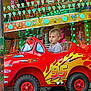 Kaelan a rejoint le concours — aidez-le/la à gagner de superbes lots ! child, toy_car, carnival, ride, amusement_park, red, flames, number_95, lights, colorful, boy, short_hair, seat, fun, outdoor, play, entertainment, vehicle, smile, young