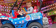 Kaelan participe au concours pour gagner de l'argent avec cette photo : child, amusement_park, ride, paw_patrol, toy_car, colorful, lights, cartoon, indoor, entertainment, playful, young_boy, vehicle, fun, decorations, amusement_ride, smiling, clothing, wheel, seat