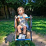 child, park, playground, spring_rocker, grass, tree, sunlight, shoes, shorts, shirt, outdoor, nature, play, toy, summer, daylight, person, cute, expression, recreation