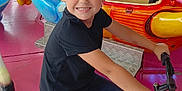 Thiago participe au concours pour gagner de l'argent avec cette photo : child, boy, bicycle, smiling, amusement_park, ride, colorful, playful, lights, black_bicycle, short_hair, casual_clothing, indoor, fun, happy, toy_ride, pink_floor, person, young, entertainment